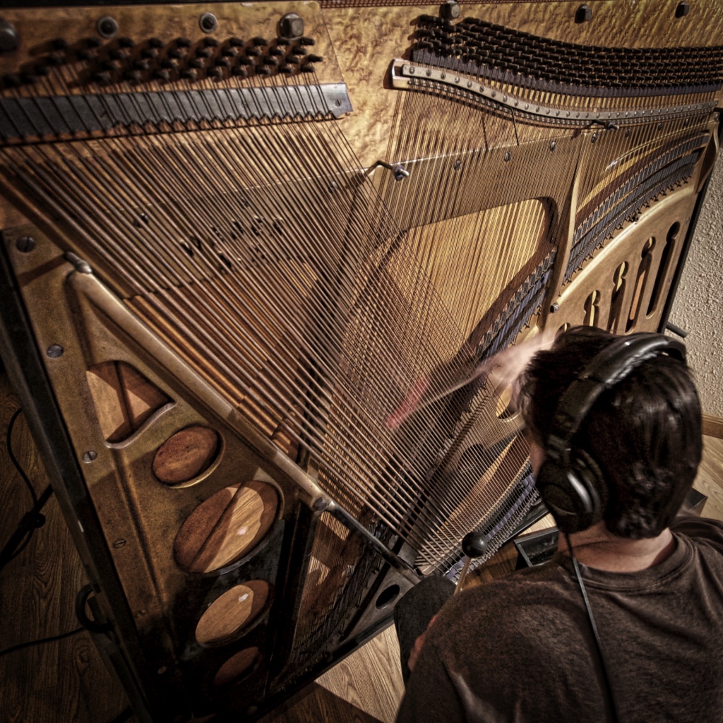 A sound artist performs a piano soundboard with a friction mallet.