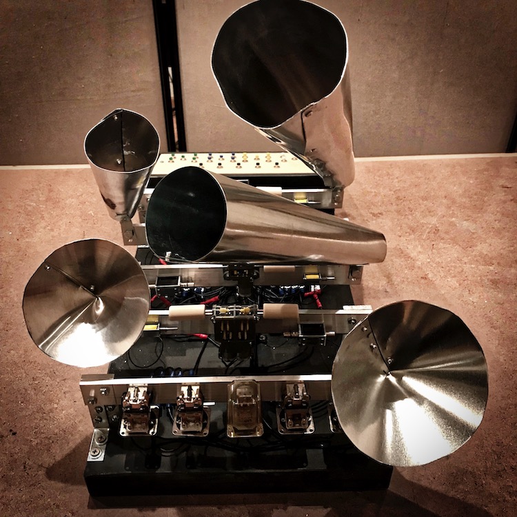 Mechanical soundmaking device with metal horns, plates, and electrical components mounted on a frame.