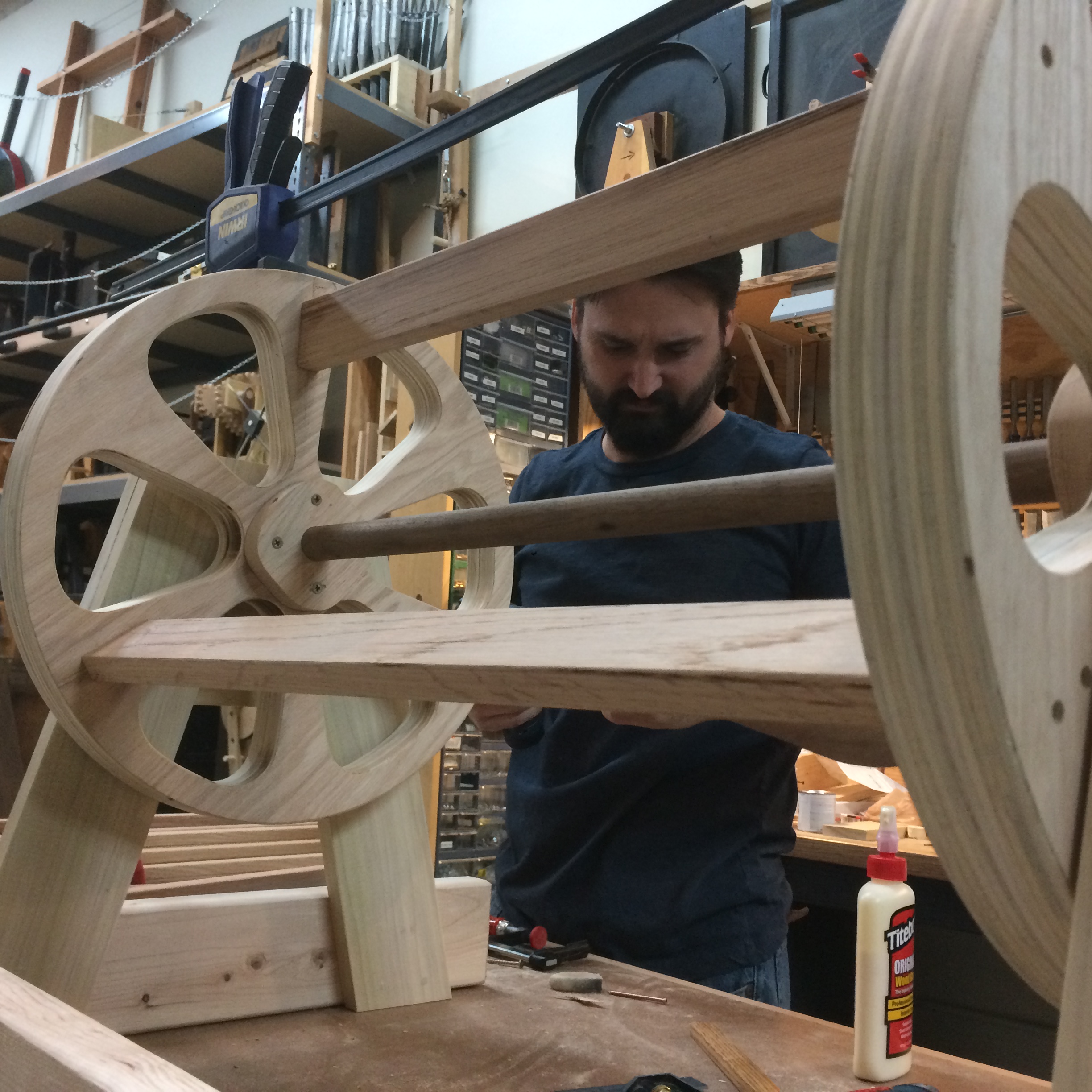 Person assembling a wooden mechanical structure in a workshop.
