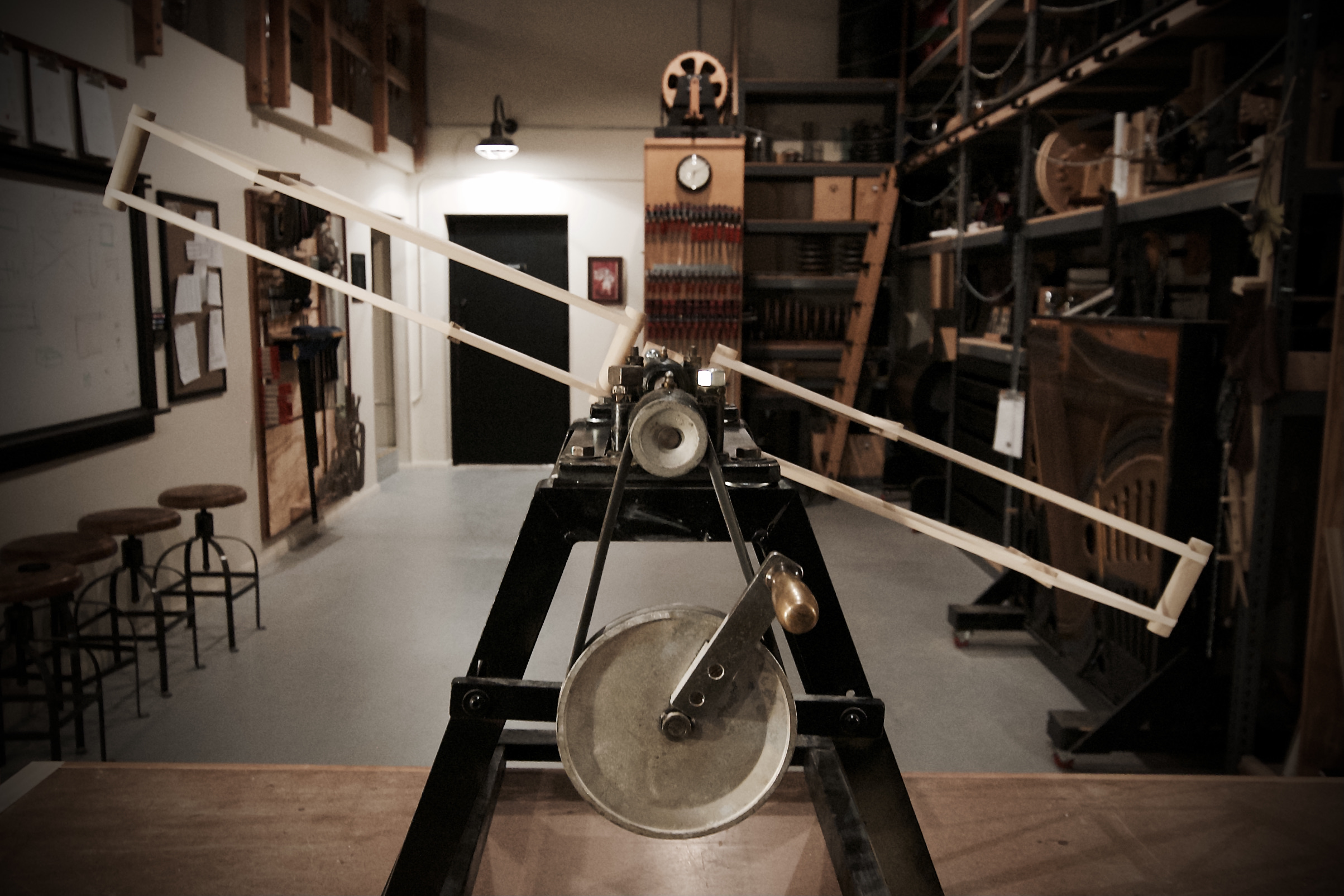 Mechanical device with long wooden arms mounted on a metal frame inside a workshop.